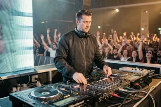 DJ français reconnu derrière ses platines sur scène de club avec foule en arrière-plan